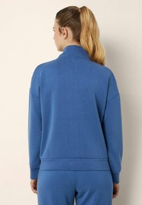 Felpa blu realizzata in tessuto morbido, con colletto alto, spalle scese e vita aderente, abbinata a pantaloni coordinati.