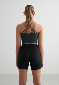 Black ribbed athletic crop top with crisscross straps, paired with high-waisted, black ribbed shorts. Smooth texture, minimal branding.