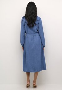 Blue long-sleeve dress with a cinched waist, textured fabric, and a flowing skirt. Features gathered cuffs and a clean, simple design.