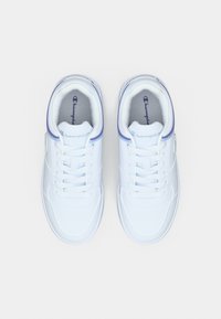 Ζευγάρι λευκά αθλητικά παπούτσια Champion με μωβ λεπτομέρειες και κορδόνια, σε λευκό απλό φόντο, φωτογραφημένα από ψηλά.