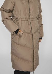Long manteau rembourré marron avec fermeture éclair à l'avant, taille élastiquée, poches latérales et poignets côtelés, avec une texture lisse et un motif matelassé.