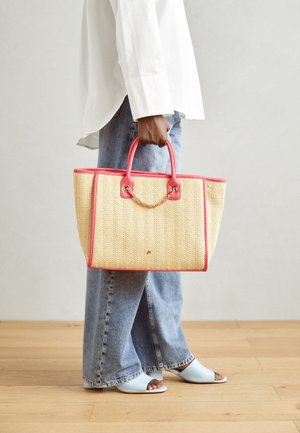 Sac en toile tressée avec des accents et des poignées roses, présentant des détails en chaîne dorée. Associé à des mules ouvertes bleu clair et à un jeans déchiré.