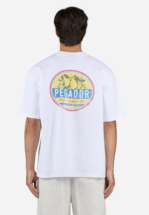 T-shirt en coton blanc à manches courtes, avec un graphique circulaire coloré au dos portant l'inscription "PEGADOR" avec un design de fruits et du texte.