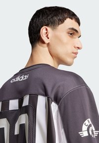 Meeste Adidas jalgpallijersey on tumashalliga, millel on valged triibud, puuvillane materjal, ümar kaelus ja tikitud logo seljal ja varrukal.