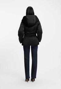 Svart pufferjacka med huva, med insnörd midja och kviltat mönster. Kombinerad med mörkblå raka jeans och svarta klackar.