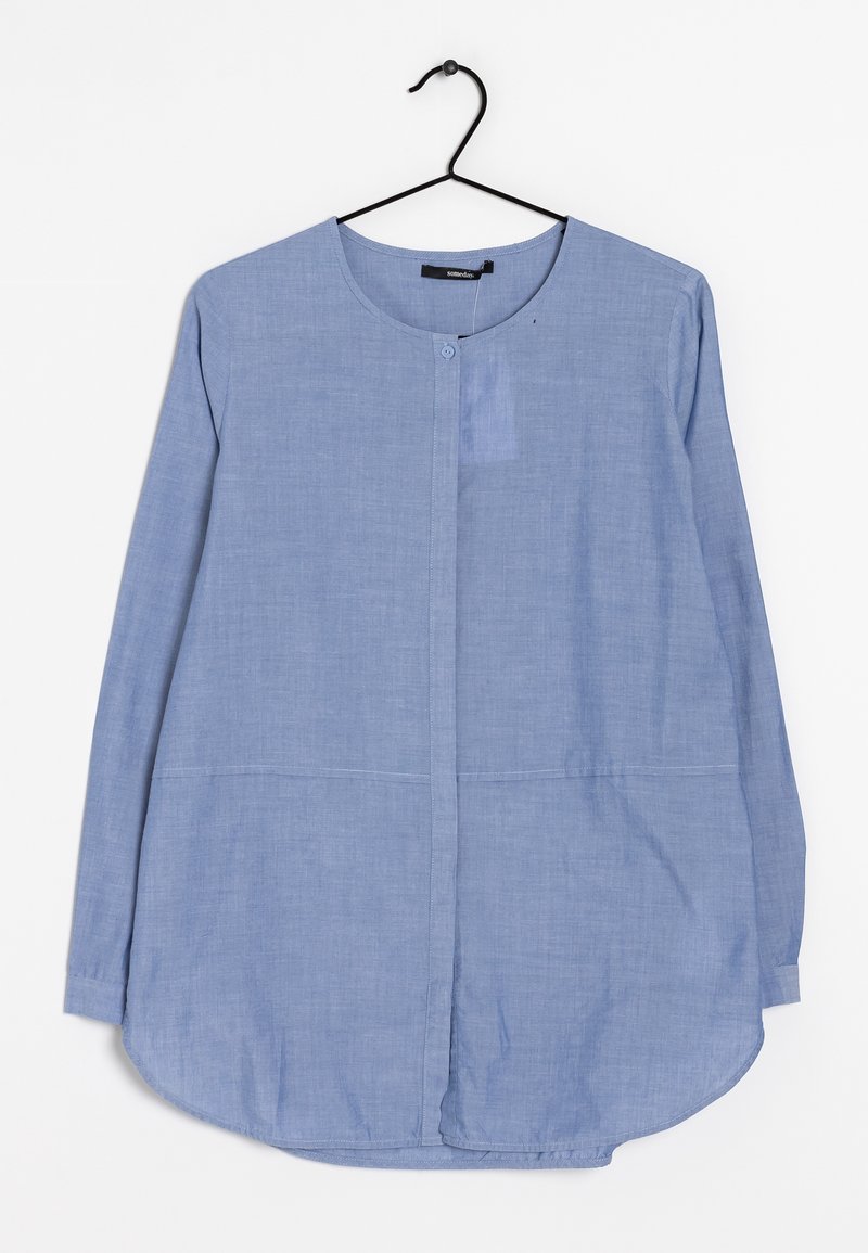 Blouse bleu clair à manches longues avec encolure ronde, boutons cachés à l'avant et ourlet légèrement arrondi, suspendue sur un cintre noir sur fond blanc.