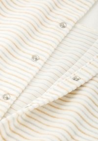 Tela blanca con suaves rayas horizontales beige; cuenta con broches plateados y una superficie texturizada, resaltando un diseño acogedor y ligero.