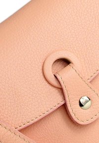 Perzikkleurige leren portemonnee met een gestructureerd oppervlak, voorzien van een ronde metalen drukknopsluiting, gestikte accenten en een eenvoudig, strak ontwerp.