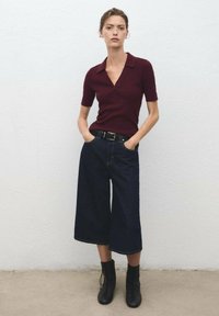 Polo à manches courtes bordeaux, large culotte en denim sombre et bottines noires à lacets. Texture lisse avec un design structuré.