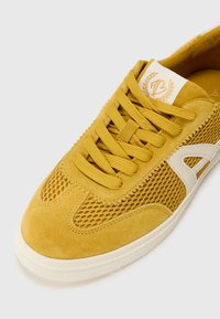 Žlté tenisky s kombináciou semišu a sieťoviny, okrúhlymi šnúrkami, bielym logom a textúrovanou podrážkou pre dobrú priľnavosť.