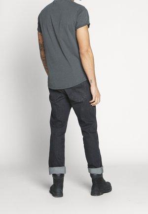 Chemise grise à manches courtes associée à un jean en denim foncé, avec des revers de manches retroussés et une coupe droite. Les chaussures sont des bottes noires.