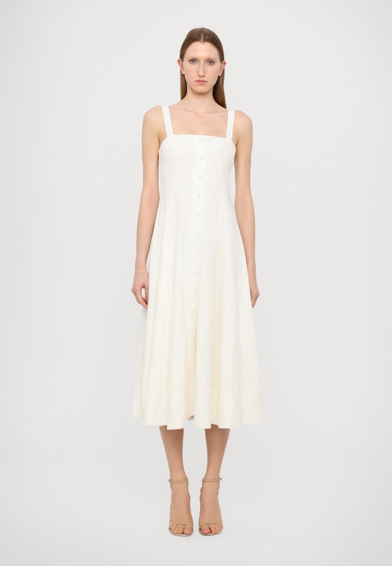 Vestido midi blanco de lino con tirantes anchos, botones frontales y un corte holgado, con una textura suave y una falda ligeramente acampanada.