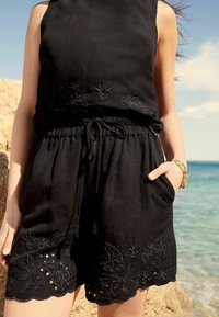 Ensemble en lin noir en deux pièces, comprenant un haut sans manches avec des broderies tonales complexes et un short avec un ourlet festonné et une taille à cordon.