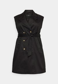 Robe noire sans manches avec un design croisé, des boutons dorés et une ceinture nouée à la taille. Fabriquée en tissu lisse avec deux poches avant.