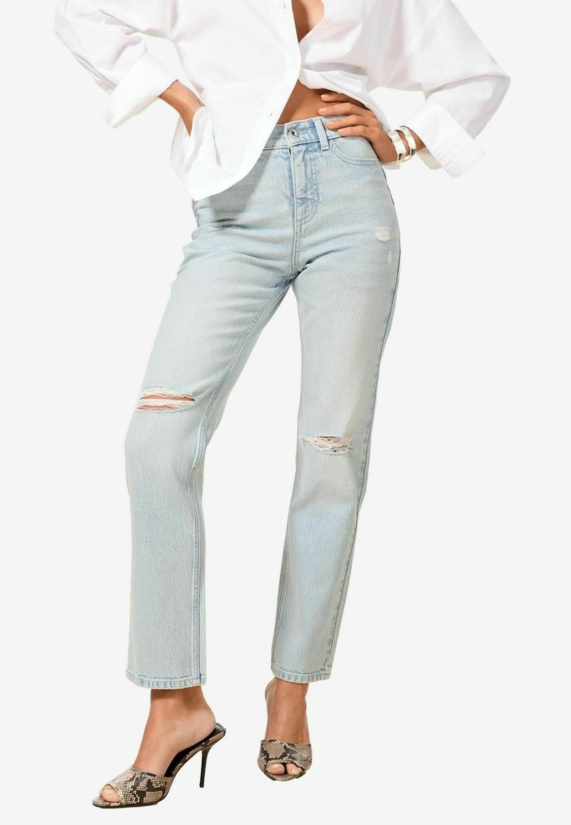 Jeans azzurri chiari a vita alta con strappi strappati sulle ginocchia, taglio dritto affusolato e orlo pulito, abbinati a sandali con tacco a stiletto in stampa serpente.