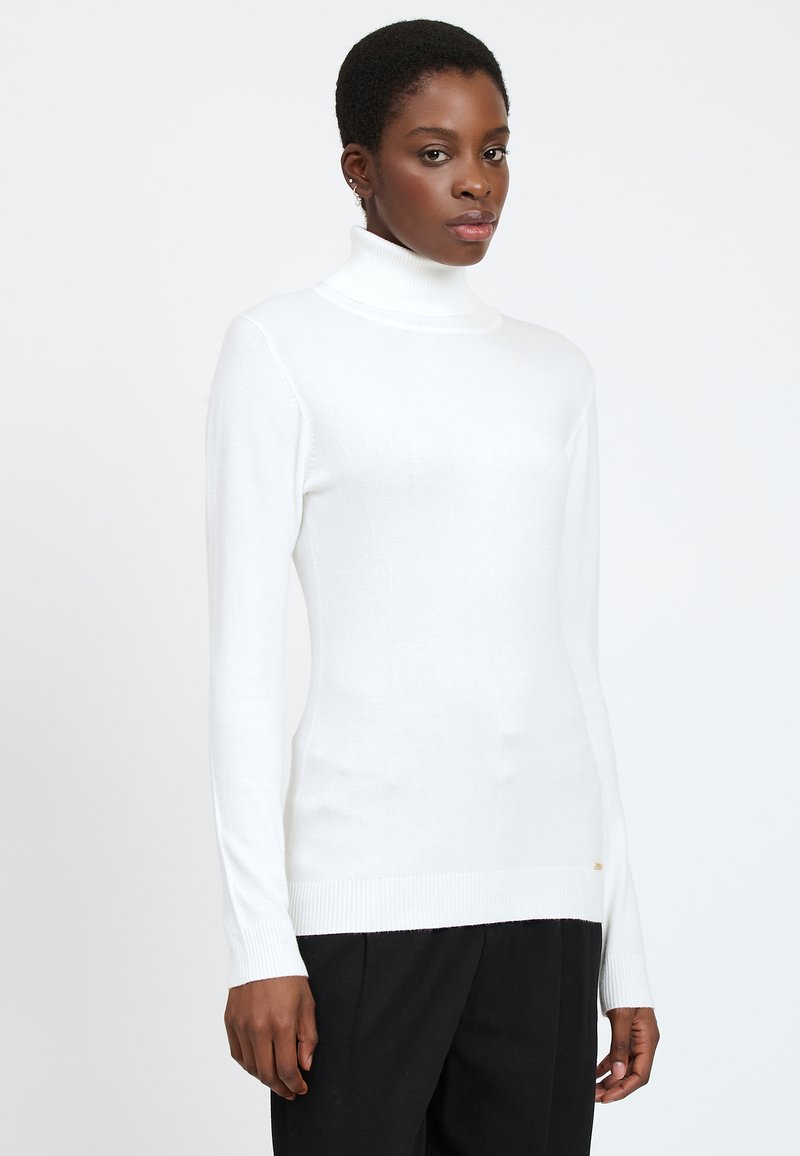 Un pull à col roulé blanc en matériau doux, avec des manches longues et des accents côtelés au col et à l'ourlet.
