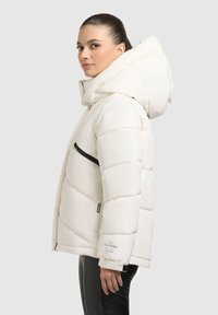 Bílá péřová bunda s velkou kapucí, prošívaným designem, černou kapsou na zip a detailem loga na rukávu. Hladká, lesklá textura.