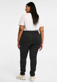 Svarta tajta jeans med hög midja och bakfickor, ihop med en enkel vit t-shirt och ljusa sneakers. Slät textur.