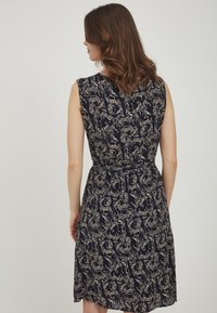 Mornarska obleka z oprijetim zgornjim delom in razširjenim krilom, ki ima zlat vzorec živali in abstraktne motive, brez rokavov in z pasom.