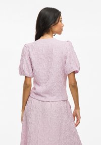 Top texturizzato rosa pallido con maniche a sbuffo, con scollatura rotonda e vita aderente, abbinato a una gonna coordinata.