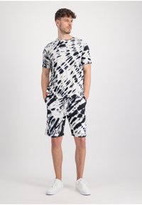Crno-bijeli tie-dye pamučna majica s kratkim rukavima i okruglim izrezom, u kombinaciji s odgovarajućim tie-dye kratkim hlačama, završena bijelim tenisicama.