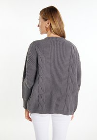 Maglione grigio a maglia con motivo a trecce e dettagli a coste. Vestibilità ampia con spalle cadenti, abbinato a pantaloni bianchi. Texture morbida, maniche di lunghezza media.