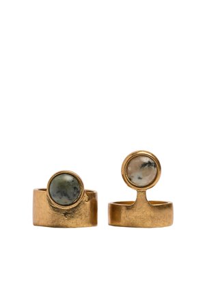 Dwa złote pierścienie z szerokimi obrączkami, każdy z okrągłym, wypolerowanym szaro-zielonym kamieniem osadzonym w oprawie.