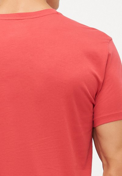 T-shirt κοντομάνικο, με λαιμόκοψη crew-neck σε κοραλλί χρώμα, φτιαγμένο από μαλακό ύφασμα με λεία υφή και άνετη εφαρμογή, παρουσιάζοντας έναν απλό σχεδιασμό.