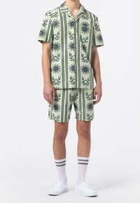 Kortärmad skjorta med knappar och matchande shorts i ljusgrön med marinblå blommönster och ränder. Vita sneakers och randiga strumpor.