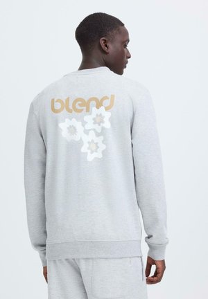 Grau melierter Baumwoll-Sweatshirt mit "blend"-Logo in Gold und floralem Print auf der Rückseite. Rundhalsausschnitt und gerippte Bündchen. Legerer Schnitt.