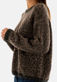 Pull en imprimé léopard dans des nuances de marron avec un tissu doux et texturé. Présente un col rond et des poignets et un ourlet côtelés.