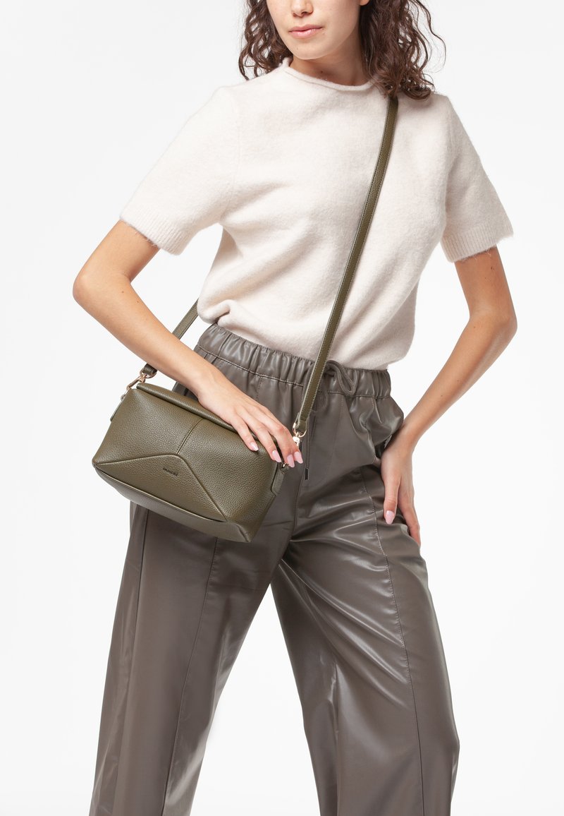 Olivenfarvet, struktureret læder crossbody taske med angular design, gyldent hardware og en justerbar rem, parret med let sweater og grå bukser.