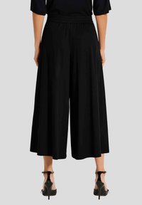 Zwarte wijde broek gemaakt van een zachte, vloeiende stof met een elastische tailleband, gecombineerd met zwarte schoenen met hoge hakken en bandjes.