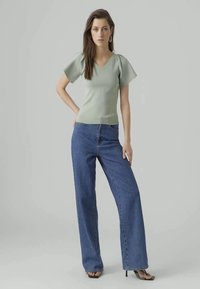 Light green fitted top with short puffed sleeves paired with high-waisted, wide-leg blue jeans and black heels. Smooth textures and casual style.