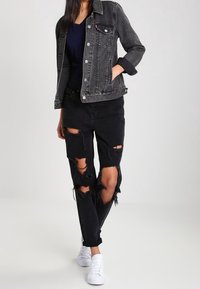 Svart denimjacka med klassisk skärning och silverdetaljer, kombinerad med slitna svarta jeans med stora hål och vita sneakers.