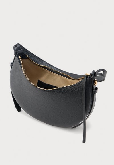 Μαύρη δερμάτινη τσάντα σε σχήμα ημισελήνου με υφή, χρυστό φερμουάρ και μπεζ εσωτερικό, με ρυθμιζόμενο λουρί και διακοσμητικά δερμάτινα τσοκ.