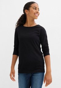 Top in cotone nero a maniche lunghe con scollo rotondo, silhouette aderente e polsini arrotolati, abbinato a jeans in denim blu.