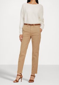 Beige bomullbyxor med rak passform, i kombination med en vit oversized tröja och ett brunt läderbälte. Inkluderar bruna strapsandaler.