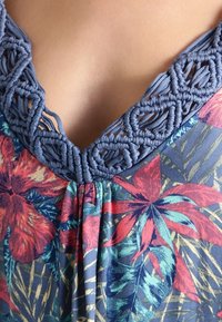 Haut à motifs floraux avec encolure en macramé bleue ; présente des teintes vives de rouge, vert et jaune sur un fond sombre ; tissu léger.