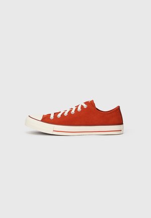 Red suede low-top sneaker with white laces, rubber toe cap, and cream sole featuring red stripes along the side. Smooth texture overall.