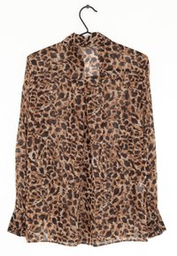 Průhledná hnědá blůza s leopardím potiskem, dlouhými rukávy, knoflíkovými manžetami a volným střihem. Visí na černém ramínku na bílém pozadí.