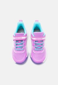 Ζευγάρι μοβ και πετρόλ παιδικά αθλητικά παπούτσια με αυτοκόλλητες λουρίδες, με την ένδειξη "GEOX", σε λευκό φόντο.