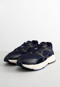 Navy blue athletic shoes featuring a mix of leather and mesh materials, a thick white sole, and light blue accents on the laces and sides.