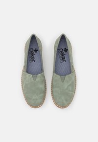 Ljusgröna slip-on skor med en texturerad läderövre del, elastiska V-formade insatser och en vävd korksåle. Inuti finns en marinblå randig foder.