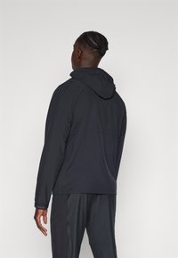 Kapuutsiga jope, mis on täiesti must ja valmistatud kergest materjalist. Omab pikaid varrukaid ja elastseid mansette. Puhtad, lihtsad jooned ilma mustriteta.