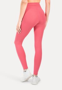 Leggings rosa ad asciugatura rapida con vita alta, caratterizzati da una texture liscia e una vestibilità atletica, abbinati a sneakers bianche.