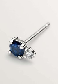 Gema azul redonda y piedra clara más pequeña engastadas en configuraciones de garra de plata, unidas a una varilla recta para un diseño de pendiente.
