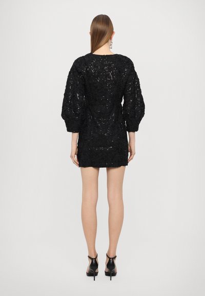 Black short dress featuring textured fabric with floral patterns, long puffed sleeves, and a fitted silhouette, paired with high-heeled shoes.