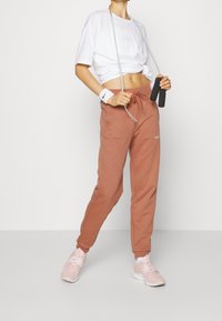 Valkoinen lyhythihainen t-paita, jossa on "Calvin"-logo, yhdistettynä ruosteenvärisiin verkkareihin ja vaaleanpunaisiin urheilukenkiin. Mukana hyppynaru ja rannebant.