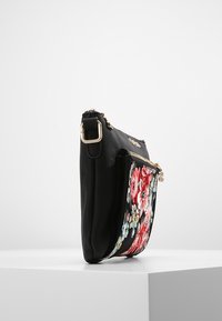 Czarna skórzana torebka z haftowanym kwiatowym wzorem na przedzie, elementami w złotym kolorze oraz zamkiem błyskawicznym. Widok z boku podkreślający jej smukły profil.